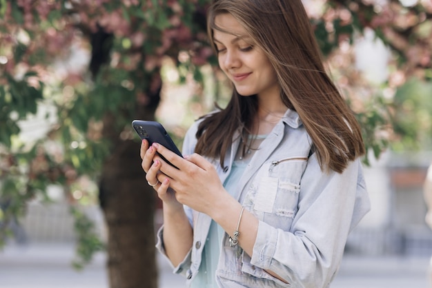 Mujer alegre mirando el teléfono móvil en la calle la gente urbana con teléfono móvil en la mano