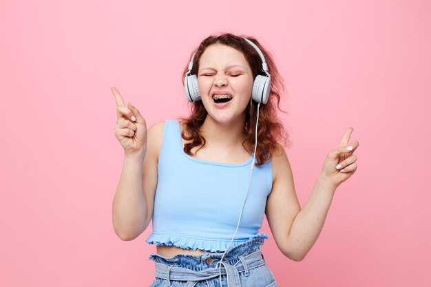 Mujer alegre con música de auriculares posando fondo rosa