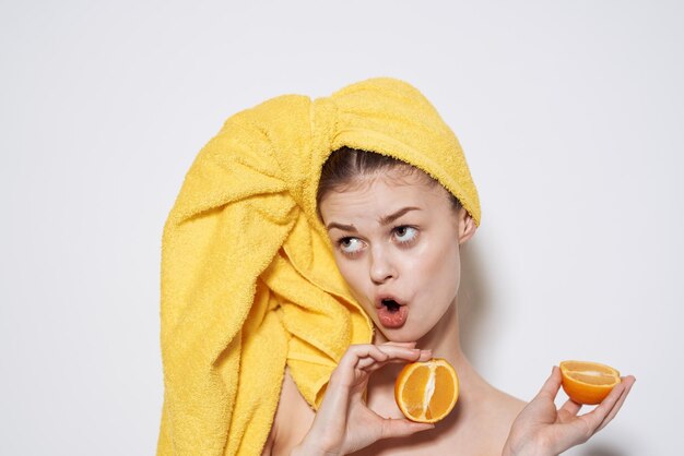 Mujer alegre con naranjas de hombros descubiertos sosteniendo una toalla en la cabeza con la piel limpia