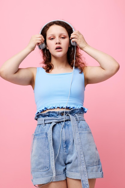 Mujer alegre en pantalones cortos de mezclilla usando auriculares tecnología de entretenimiento de moda inalterada