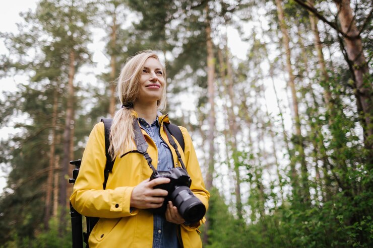 Mujer alegre de pie en el bosque de primavera con cámara digital