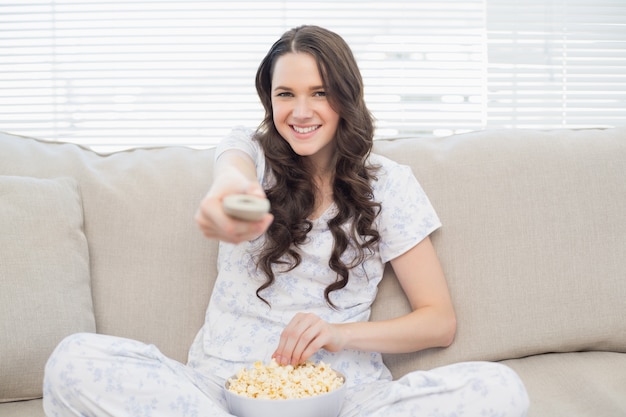 Mujer alegre en pijama con palomitas mientras mira tv