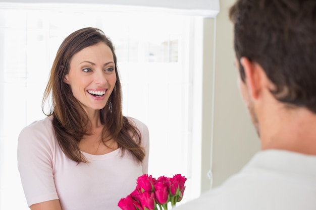 Mujer alegre que mira al hombre con las flores