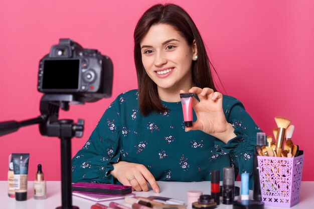 Mujer alegre que muestra productos cosméticos mientras graba videos y da consejos