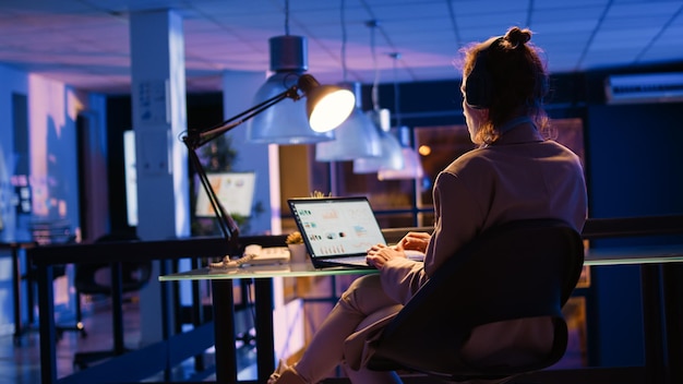 Mujer alegre que trabaja con auriculares en la oficina de inicio que planifica el desarrollo corporativo con un informe económico para aumentar las ganancias comerciales. Empleada analizando estadísticas. Disparo de mano.