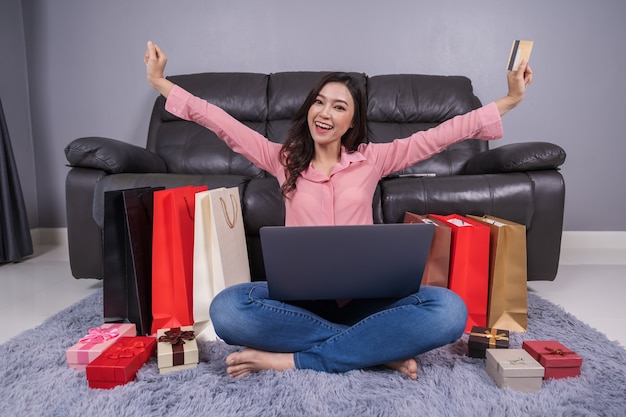 Mujer alegre que usa la computadora portátil para realizar compras exitosas en línea con tarjeta de crédito en la sala de estar