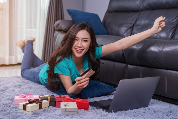 Mujer alegre que usa la computadora portátil para realizar compras exitosas en línea con tarjeta de crédito en la sala de estar