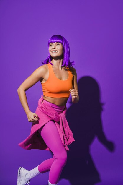 Foto mujer alegre con ropa deportiva colorida corriendo contra un fondo morado