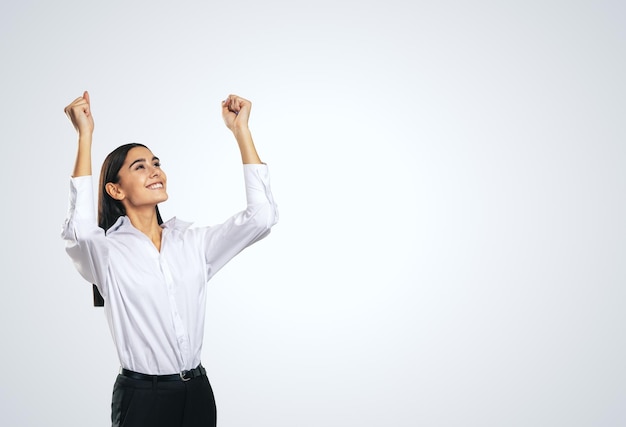 Mujer alegre y satisfecha con camisa blanca con las manos levantadas mostrando su ganador de poder y el concepto de logro aislado en un fondo gris claro con un lugar vacío para su maqueta de texto o logotipo