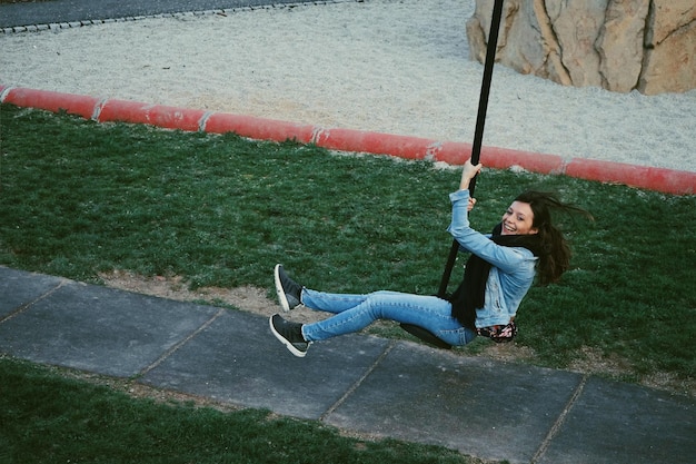 Mujer alegre sentada en el columpio en el patio de recreo