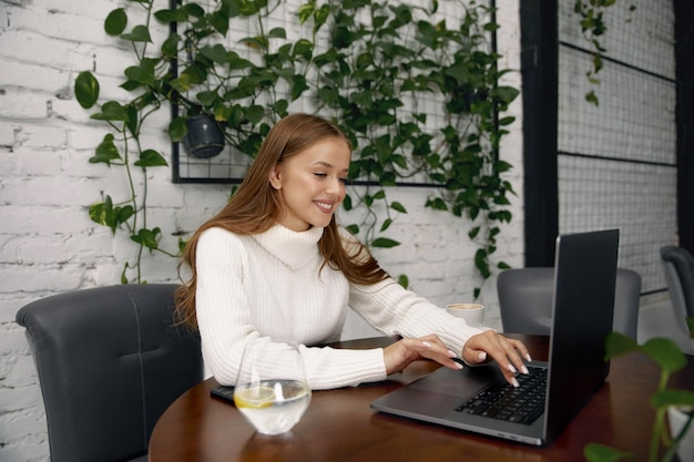 Mujer alegre sentada en la mesa estudiando usando una computadora portátil leyendo un libro navegando por Internet