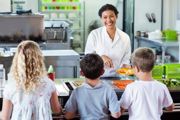 Mujer alegre sirviendo comida a escolares