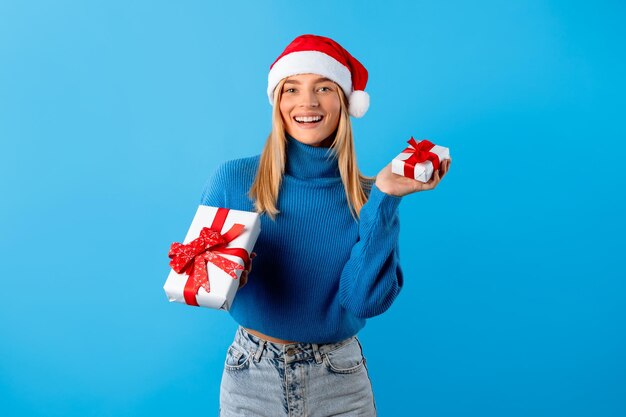 Foto mujer alegre con sombrero de santa con regalos de navidad de fondo azul