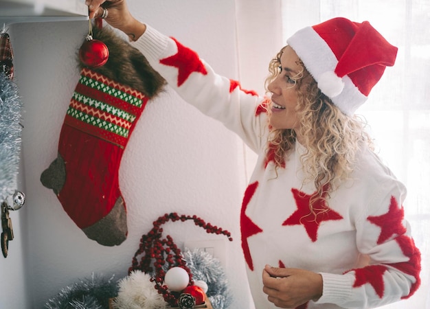 Mujer alegre sonríe y disfruta de decorar el apartamento con adornos navideños Mujeres jóvenes usan sombrero de santa claus y se divierten durante la temporada de vacaciones de diciembre Una joven en ocio interior