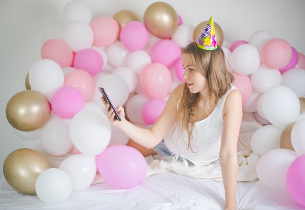 Mujer alegre sonriendo y tomando selfie en celular con globo