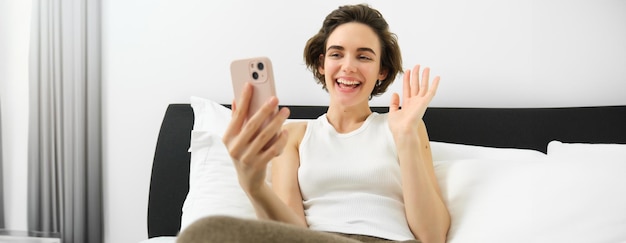 Foto mujer alegre y sonriente descansando en la cama se conecta a una videollamada en línea mientras está acostada en el dormitorio hablando