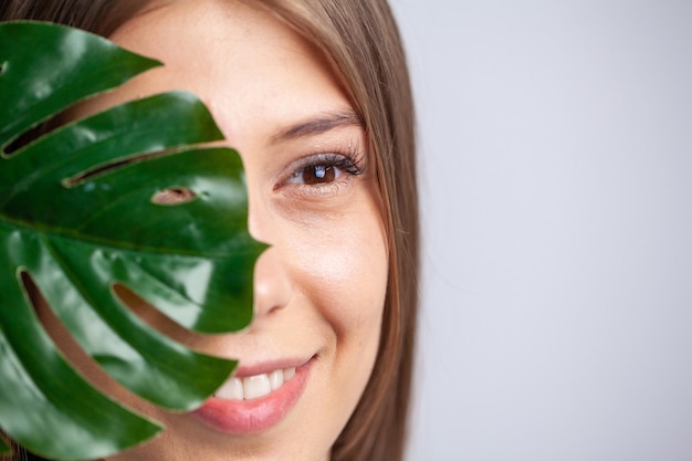 Mujer alegre con una sonrisa sostiene una hoja de una flor cerca de la cara