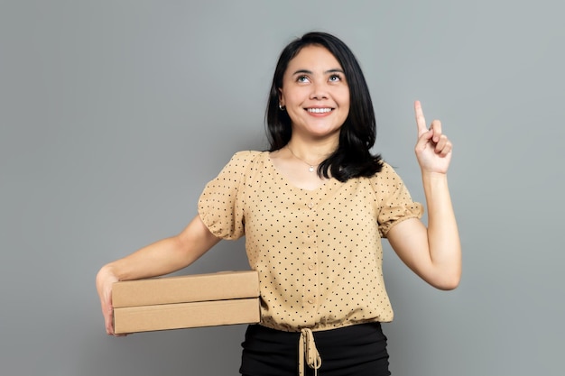 Mujer alegre sosteniendo como una caja de pizza apunta y mira hacia arriba