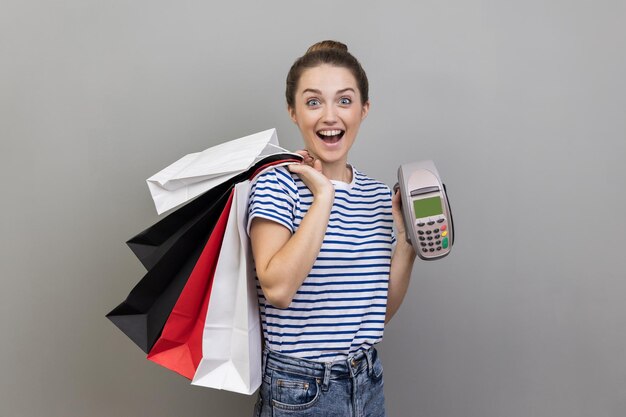 Mujer alegre sosteniendo y mostrando terminal de pago y bolsas de compras expresando emoción