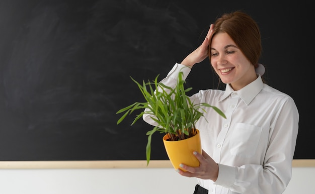 Mujer alegre sosteniendo una planta cerca de una pizarra