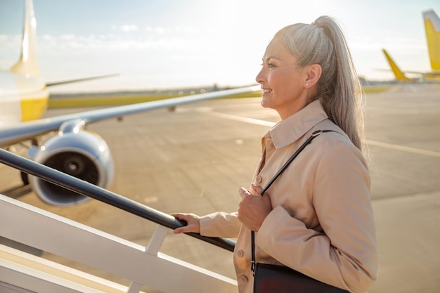 Mujer alegre subiendo las escaleras del avión en el aeropuerto