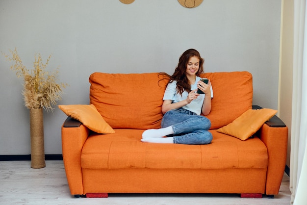 Foto mujer alegre con un teléfono en sus manos en el sofá apartamentos foto de alta calidad