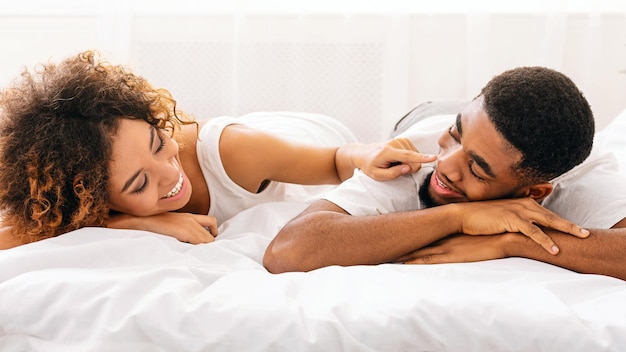 Mujer alegre tocando la nariz de su marido en la cama