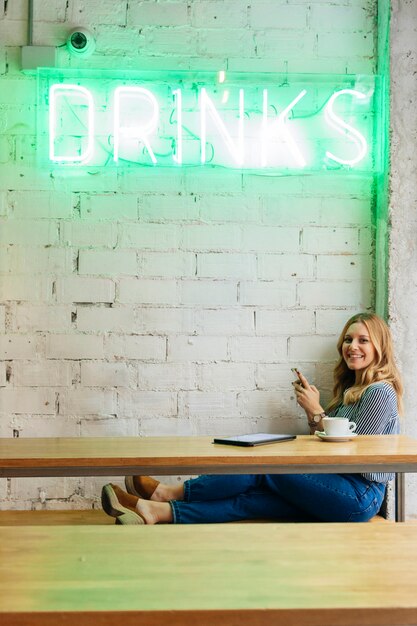 Mujer alegre tomando una copa en la cafetería moderna