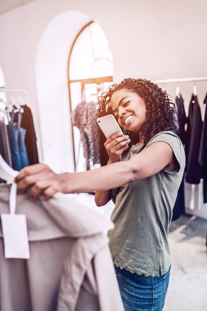 Mujer alegre tomando fotos de ropa en tienda