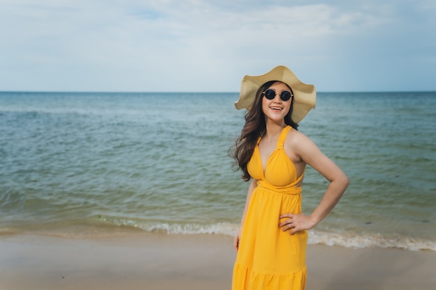 Mujer alegre en vestido amarillo disfrutando en la playa del mar