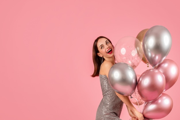 Mujer alegre en un vestido plateado brillante se ríe de corazón agarrando un montón de metálico brillante y