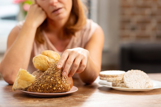 Mujer alérgica al gluten tomando bollo con semillas, patatas fritas sin gluten