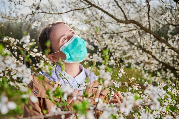 Mujer alérgica que sufre de alergia estacional en primavera posando en un jardín en flor en primavera