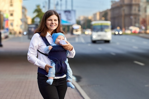 Mujer alimenta a niño en cabestrillo cerca del tráfico mientras camina