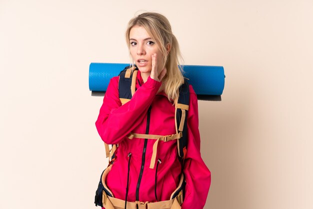 Mujer alpinista con una gran mochila sobre pared aislada susurrando algo