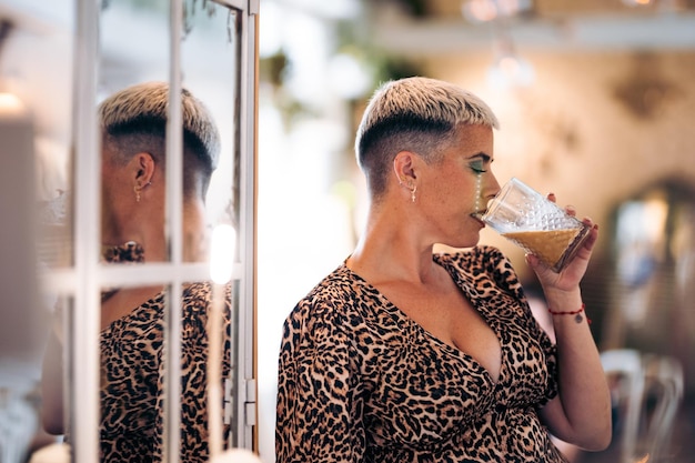 Foto mujer alternativa con cabello corto bebe una taza en un bar y su reflejo