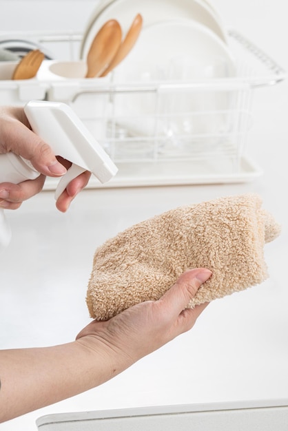 La mujer ama de casa está haciendo la limpieza de primavera en la cocina de la casa usando un trapo, rociando un limpiador de botellas para limpiar la superficie de la mesa.