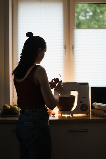 Mujer ama de casa horneando en casa usando un mezclador planetario de cocina en una cocina acogedora