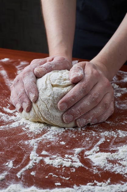 La mujer amasa la masa con las manos. Manos femeninas y masa cruda sobre un fondo de madera. Masa de pizza o productos horneados. Hornear pan, pizza, pasta.