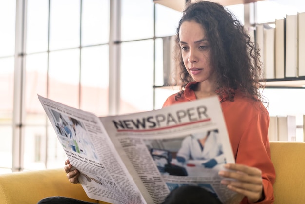 Mujer de América Latina leyendo el periódico en el sofá en casa