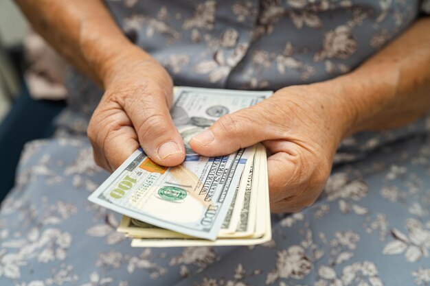Foto mujer anciana asiática sosteniendo y contando billetes de dólares estadounidenses dinero en el bolso problema de ahorro de pobreza en la jubilación