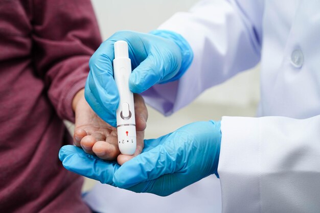 Mujer anciana asiática usando una pluma lancet en el dedo de un paciente anciano para comprobar el nivel de azúcar en la sangre de la muestra para el tratamiento de la diabetes