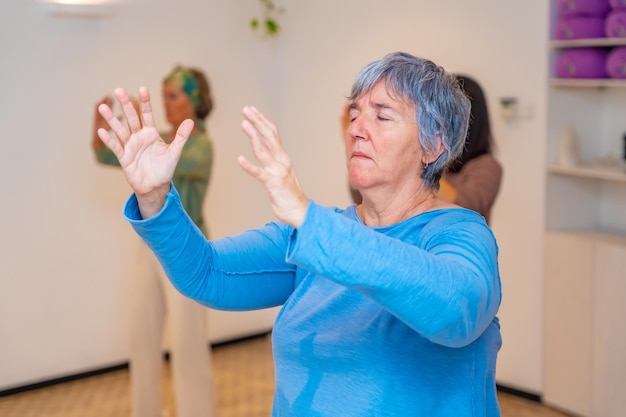 Foto mujer anciana cerrando los ojos y levantando los brazos durante la clase de qi gong