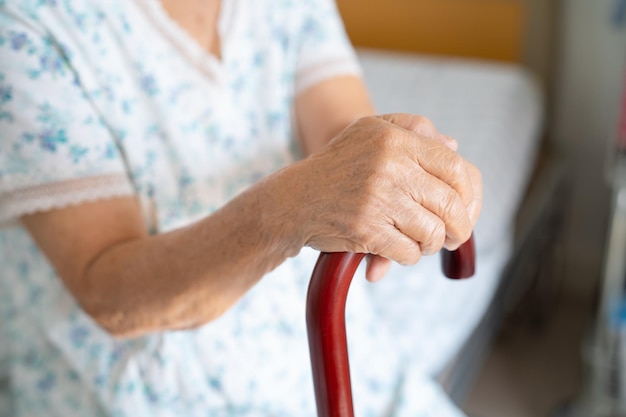 Mujer anciana con discapacidad asiática sosteniendo un bastón de madera, caña, mango redondo, ayuda para caminar para ayudar a caminar