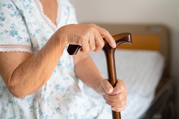 Mujer anciana con discapacidad asiática sosteniendo un bastón de madera, caña, mango redondo y caminando