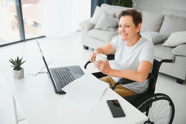 Mujer anciana positiva en silla de ruedas que trabaja en una computadora portátil independiente de TI en línea