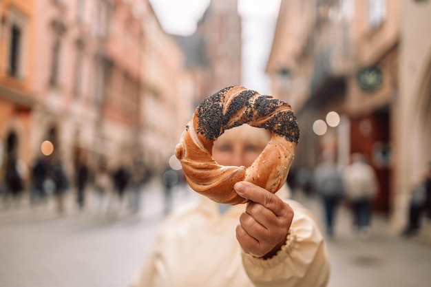 Mujer anciana sosteniendo prezel bocadillo tradicional polaco contra la vista del centro de la ciudad vieja en Cracovia