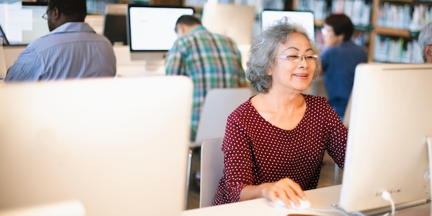 Mujer anciana usando una computadora en una biblioteca Sénior centrado trabajando en un escritorio Aprendizaje y tecnología para adultos mayores en un espacio público con espacio de copia Conceptos de ancianos y tecnología