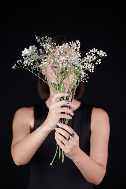 Mujer en anillos de plata sosteniendo flores contra la cara mientras presenta nueva colección de joyas negro ...