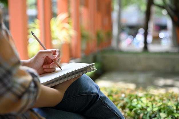 Una mujer anotando ideas o planificando su proyecto en un cuaderno mientras se relaja sentada en el parque